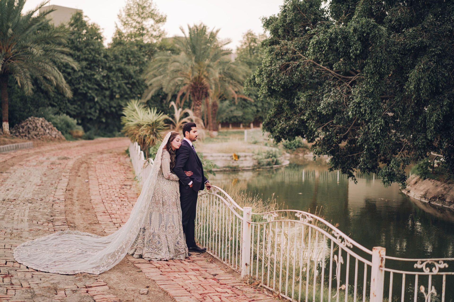 Couple by a palm-lined lakeside path during an outdoor pre-wedding shoot in Lahore